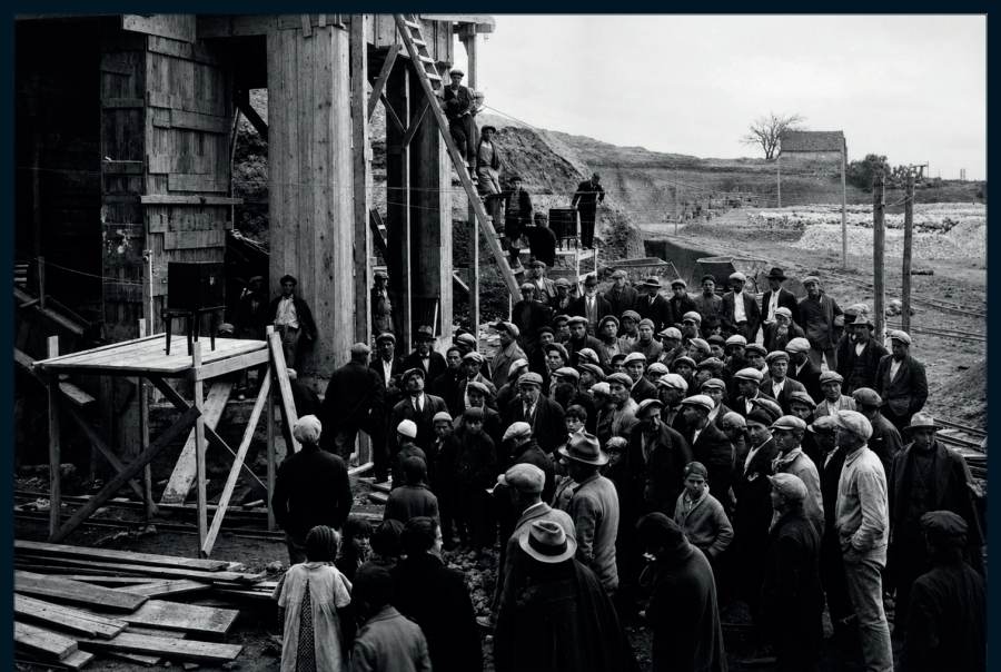 Les ouvriers, réunis à la base de la construction, écoutent un communiqué à la radio.