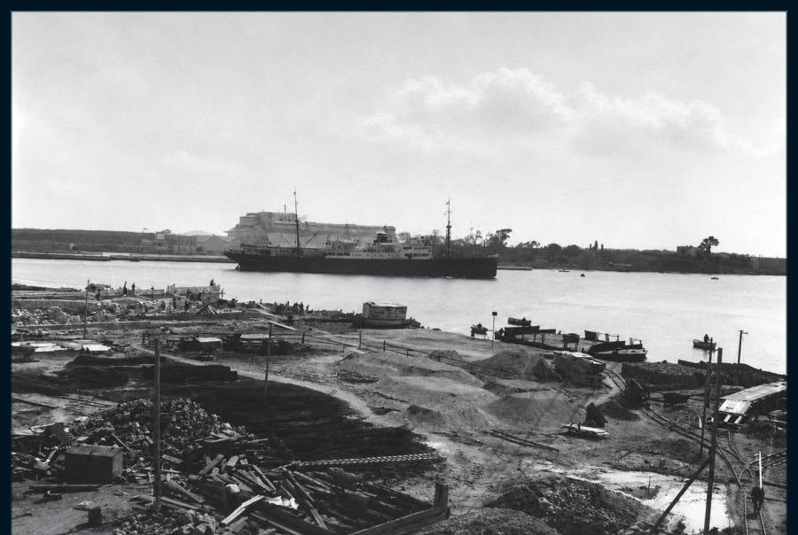 Die Baustelle wird eingerichtet; im Hintergrund ein einlaufendes Schiff und die Halle der Montedison.